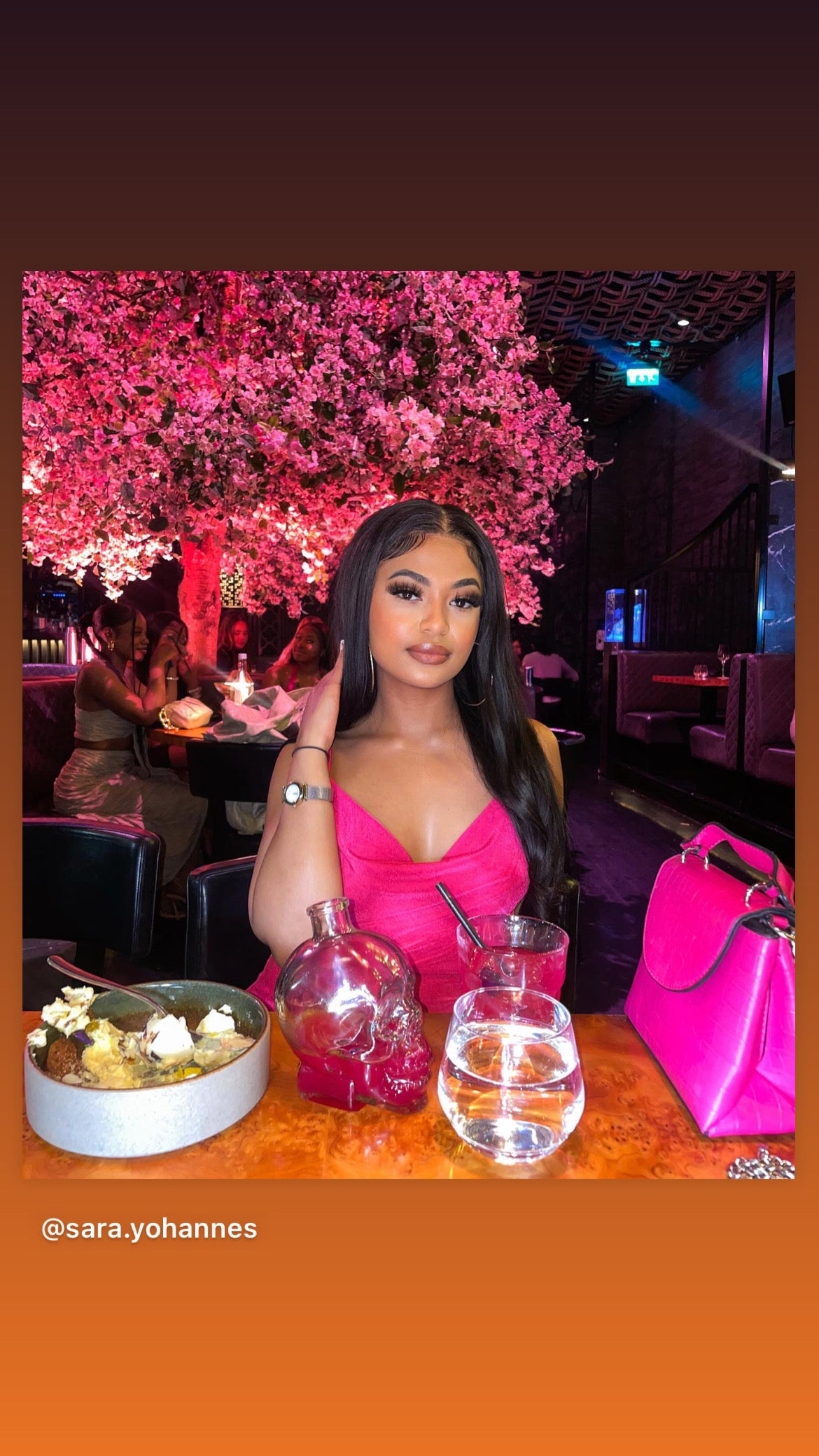 a woman sitting at a table with pink flowers
